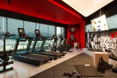 Academia com esteiras, bikes e equipamentos de musculação, paredes vermelhas e janelas panorâmicas com vista para a cidade — Imob Trindade On em Trindade, Florianópolis