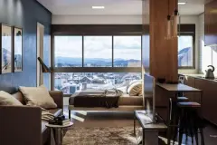 Apartamento studio com sala integrada ao dormitório, cama junto à janela panorâmica com vista para Florianópolis e balcão de cozinha com banquetas — Imob Trindade On em Trindade, Florianópolis