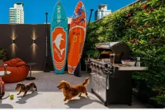 Área de lazer externa com pranchas de paddle, churrasqueira, jardim vertical e dois cachorros dachshund — Imob Trindade On em Trindade, Florianópolis
