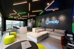Espaço de convivência interno com sofá em L, poltronas amarelas, cozinha coletiva e logo mob na parede, iluminação de LED no teto — Imob Trindade On em Trindade, Florianópolis