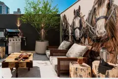 Espaço gourmet externo com mesa rústica, sofás de madeira e mural artístico com cavalos — Imob Trindade On em Trindade, Florianópolis