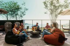 Rooftop lounge com grupo de amigos ao redor de fogueira, violão, bebidas e vista para o mar e montanhas — Imob Trindade On em Trindade, Florianópolis