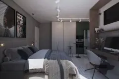 Studio com cama de casal, armário embutido, TV, escrivaninha com computador e cozinha integrada em tom escuro — Imperial Residence em Campeche, Florianópolis