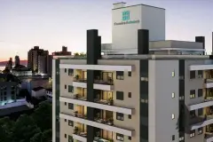 Vista aérea do edifício ao entardecer com logo Ferreira Antunes iluminado no topo e cidade ao redor — In Haus Afonso Pena em Canto, Florianópolis