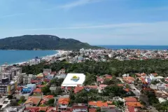 Vista aérea do bairro Ingleses com praia e vegetação, logo do empreendimento destacado no terreno — Infinity Residence em Ingleses, Florianópolis