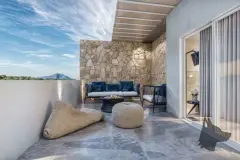 Varanda com parede de pedra rústica, sofá azul, puff e vista para morro ao entardecer — Infinity Residence em Ingleses, Florianópolis
