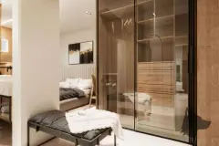 Suíte com closet de vidro e madeira, cama com roupa de cama escura e acesso ao banheiro — Infinity Residence em Ingleses, Florianópolis