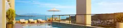 Terraço com piscina infinita, espreguiçadeiras, guarda-sol e vista panorâmica para a Baía Norte e Florianópolis — Jardim Cacupé Residence em Cacupé, Florianópolis
