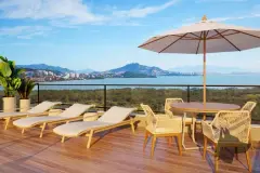 Área de lazer no terraço com espreguiçadeiras, guarda-sol e mesa com cadeiras com vista para a Baía Norte — Jardim Cacupé Residence em Cacupé, Florianópolis