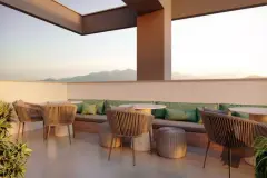 Espaço lounge no rooftop com sofás e cadeiras de vime, almofadas verdes e vista para os morros ao entardecer — Jardim de Coqueiros em Coqueiros, Florianópolis