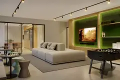 Sala de jogos com sofá modular, mesa de pebolim, TV em painel verde iluminado e área gourmet ao fundo — Jardim de Coqueiros em Coqueiros, Florianópolis
