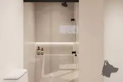 Banheiro compacto com box de vidro, chuveiro preto, nicho iluminado com produtos e vaso sanitário — Max Studios 45 em João Paulo, Florianópolis