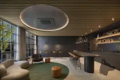 Espaço social com sofá curvo, poltrona, balcão bar com bebidas e mesa alta com tamboretes — Max Studios 177 em Pantanal, Florianópolis