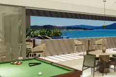 Área gourmet aberta com mesa de sinuca, mesas redondas, sofás e vista panorâmica para o mar — Maxxi View em Jurerê, Florianópolis