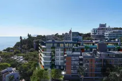 Vista aérea do empreendimento com fachada escura e verde, logotipo Modulare no topo e bairro ao redor — Maxxi View em Jurerê, Florianópolis