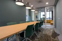 Sala de reuniões com mesa longa de madeira e cadeiras verdes, lounge amarelo ao fundo — Maxxi View em Jurerê, Florianópolis