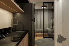 Detalhe da cozinha com cooktop, pia e geladeira preta com porta de vidro para o dormitório ao fundo — Maxxi View em Jurerê, Florianópolis