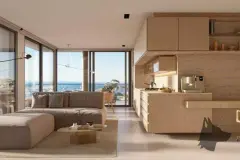 Sala de estar aberta com sofá bege, cozinha integrada em madeira clara e janela panorâmica com vista para o mar — Meraki Allure em Jurerê, Florianópolis