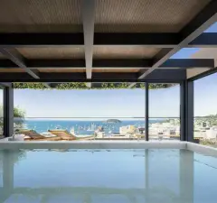 Piscina coberta em retrato com teto ripado de madeira, espreguiçadeiras e vista para o mar de Jurerê — Meraki Allure em Jurerê, Florianópolis