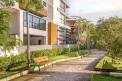 Área de lazer no térreo com caminho de pedras, banco, jardim e playground ao fundo — Meraki Allure em Jurerê, Florianópolis