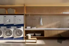 Lavanderia compartilhada com máquinas de lavar, bancada e armários em madeira clara — Meraki Allure em Jurerê, Florianópolis