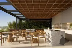 Área gourmet com mesas e cadeiras de madeira, balcão de pedra, teto ripado e jardim de bambu — Meraki Allure em Jurerê, Florianópolis