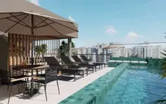 Piscina rooftop com espreguiçadeiras, guarda-sol bege, azulejos verdes e palmeiras com vista para o centro — Mirá Apartments em Centro, Florianópolis