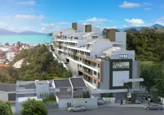 Fachada diurna do empreendimento com prédio branco e baia turquesa ao fundo — Mirante dos Corais em Coqueiros, Florianópolis