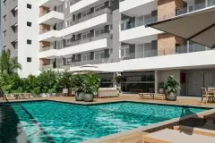 piscina fachada guarda-sol deck palmeiras espreguiçadeiras ângulo frontal — Neo Continente em Estreito, Florianópolis