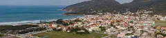 Vista aérea panorâmica da praia da Barra da Lagoa com mar azul-turquesa, casas coloridas e morro ao fundo em Florianópolis — Orla da Barra em Barra da Lagoa, Florianópolis