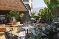 área de convivência coberta render telhado ripas madeira mesas cadeiras banco circular terracota jardim tropical pessoas ângulo alternativo — Parkside Itacorubi em Itacorubi, Florianópolis