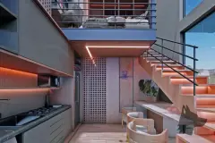 Perspectiva da sala integrada com cozinha, escada e mezanino com dormitório, vista noturna — Puerto Canas em Canasvieiras, Florianópolis