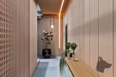 Perspectiva do corredor de entrada com painéis ripados em madeira e iluminação indireta pendente — Puerto Canas em Canasvieiras, Florianópolis