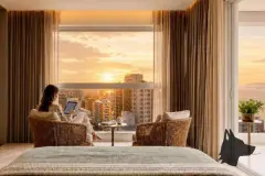 perspectiva ilustrativa suíte cama casal poltrona mesa redonda madeira janela vista panorâmica pôr do sol prédios baía Florianópolis cortinas areia — Regency Square Smart Stay em Centro, Florianópolis