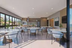 Salão de festas amplo com mesas redondas brancas, cadeiras, cozinha ao fundo e janelas panorâmicas — Saint Zambelli em Ingleses, Florianópolis
