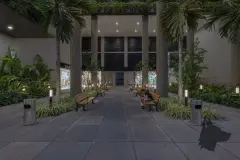 Corredor de entrada do edifício à noite com bancos, palmeiras e lojas ao fundo — Saint Zambelli em Ingleses, Florianópolis