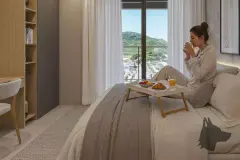 Quarto decorado com mulher tomando café da manhã na cama, janela com vista para montanhas e guarda-roupa — Saint Zambelli em Ingleses, Florianópolis
