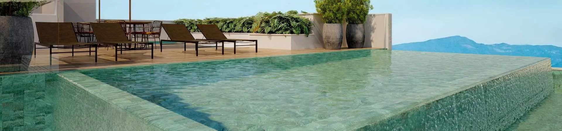 Piscina infinity no rooftop com borda de pedra verde, deck de madeira e espreguiçadeiras, vista para morros ao fundo — Seleto Carlessi em Trindade, Florianópolis