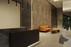 Hall de entrada com balcão de mármore escuro, sofá laranja, parede de tijolinho e luminária pendente — Seleto Carlessi em Trindade, Florianópolis