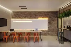 Espaço coworking com mesa longa, cadeiras laranja, parede de tijolos e letreiro neon coworking — Seleto Carlessi em Trindade, Florianópolis