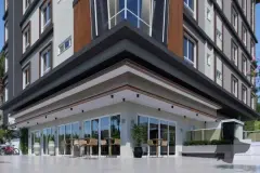 Fachada do edifício com térreo comercial envidraçado, mesas externas e detalhe de ripas de madeira — Solis em Ingleses, Florianópolis