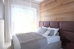Suíte com cama de casal, cabeceira de couro bordô, painel de madeira e janela com luz natural — Solis em Ingleses, Florianópolis