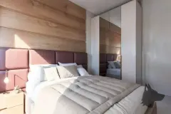 Suíte com cama de casal, cabeceira bordô, armário espelhado e painel de madeira — Solis em Ingleses, Florianópolis
