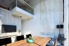 Sala de jantar duplex com mesa de madeira, parede de vidro de pé direito duplo e painel de mármore — Solis em Ingleses, Florianópolis