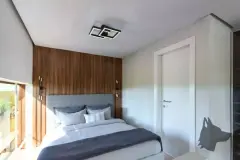 Dormitório com cama de casal, painel de madeira, plafon e porta para varanda iluminada — Solis em Ingleses, Florianópolis