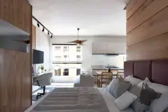 Quarto integrado com sala visto da cama, painel de madeira, sofá e cozinha americana ao fundo — Solis em Ingleses, Florianópolis