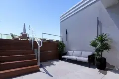 Terraço externo com escada de madeira para rooftop, sofá externo e plantas decorativas — Solis em Ingleses, Florianópolis