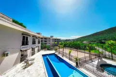 Área da piscina com espreguiçadeiras e quadra de areia ao fundo, morro com mata nativa — Summer Park Residence - Fase 2 em Vargem do Bom Jesus, Florianópolis
