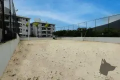 Quadra de beach tennis com areia, cercada por tela e edifício ao fundo — Summer Park Residence - Fase 2 em Vargem do Bom Jesus, Florianópolis