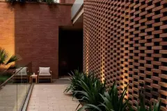 Pátio externo com parede de tijolos aparentes em relevo, poltrona de madeira e agave — Terracota em Morro das Pedras, Florianópolis
